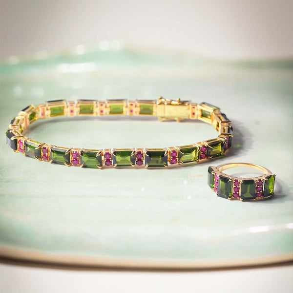 Gold bracelet and ring with green and ruby gemstones on a light green background