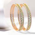 Gold bangles with emerald gemstones on a white background
