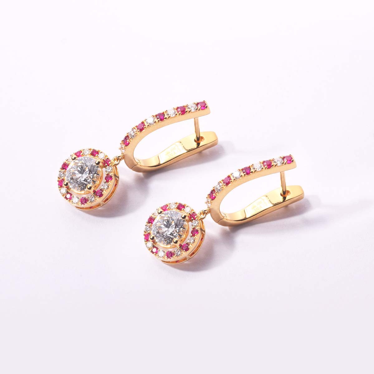 Gold hoop earrings with gemstones on a light pink background